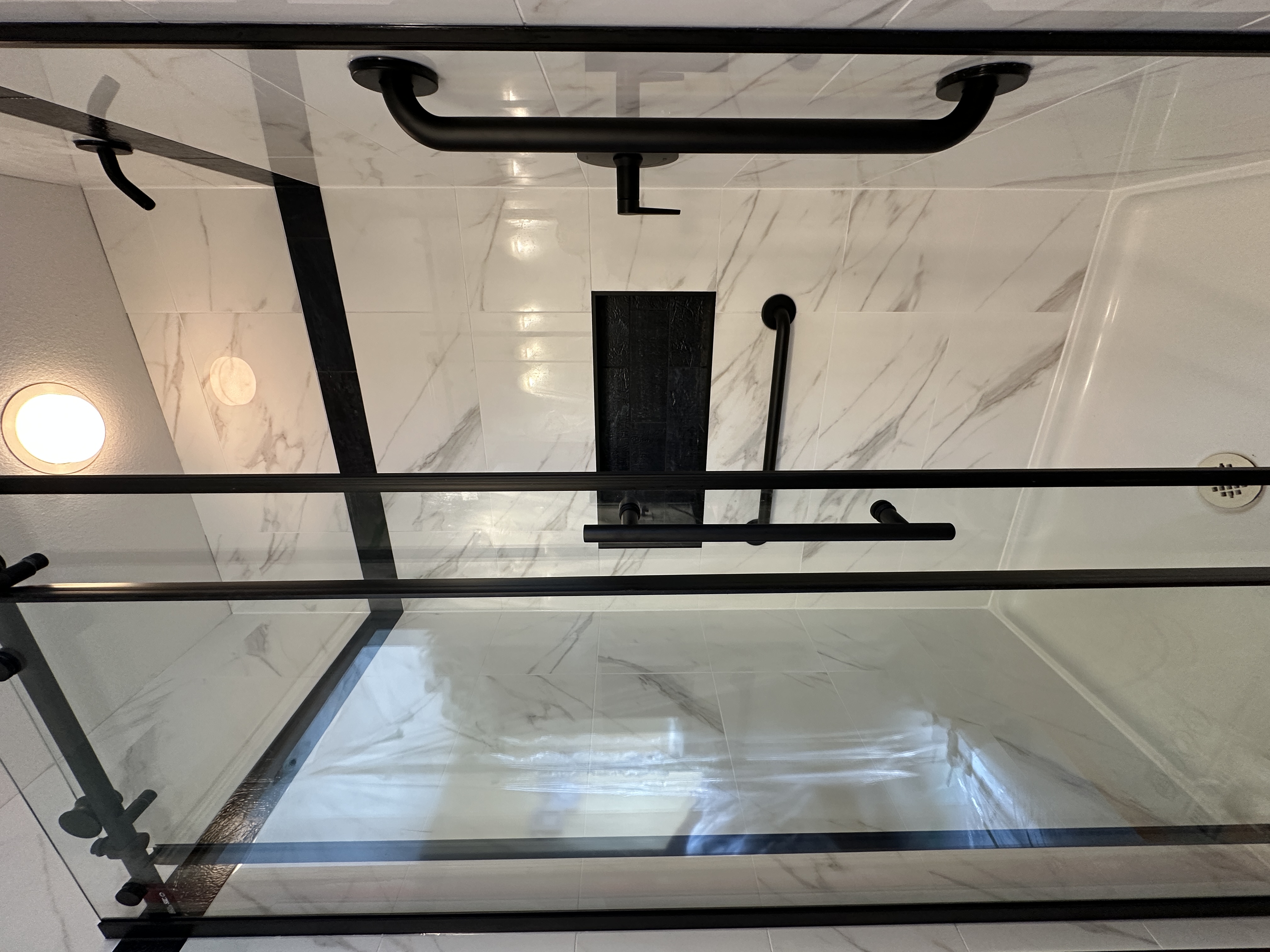 Black framed glass shower door and grab bars on the finished tub surround