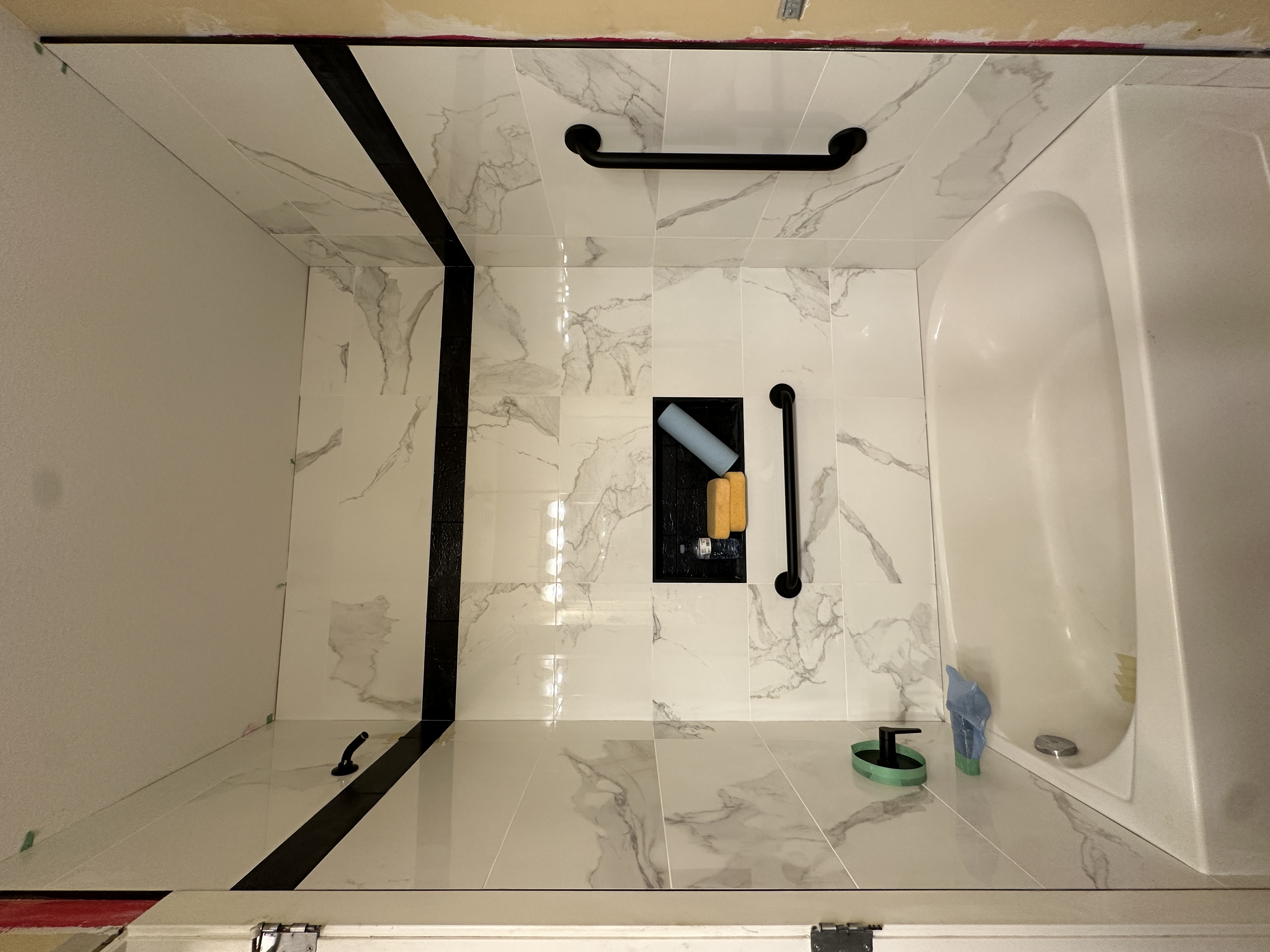 The same tub surround after the renovation, marble look porcelain tile with a black accent band